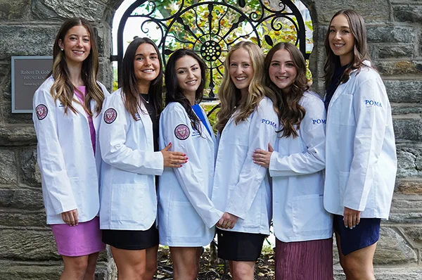 PCOM DO students wearing white coats pose for a group photo