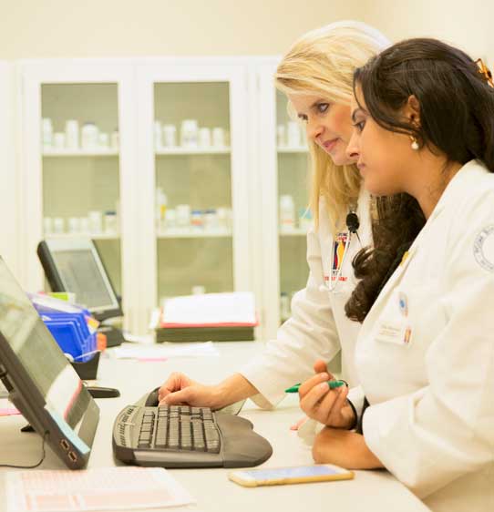 Interested in pharmacy as a career? A pharmacy professor is shown working with a student who is studying to become a pharmacist.