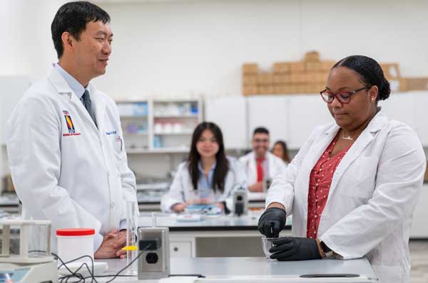 A pharmacy professor works with a pharmacy student in the lab.