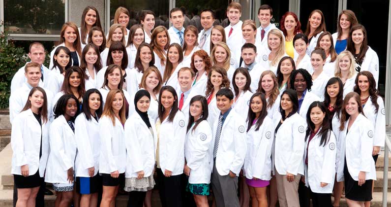 PCOM PA program students pose for a class photo wearing their white coats.