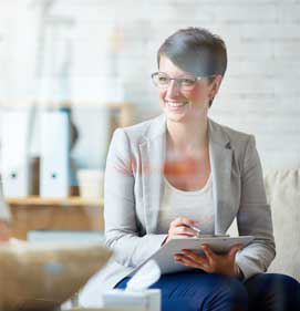 A smiling woman wearing glasses is writing in a notepad.