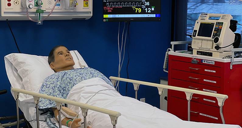 High fidelity mannequin A PCOM CLAC Sim Center high fidelity mannequin in a hospital bed in a simulation hospital room