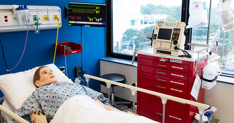 A simulation room at PCOM's CLAC with a high fidelity mannequin laying in bed in front of windows