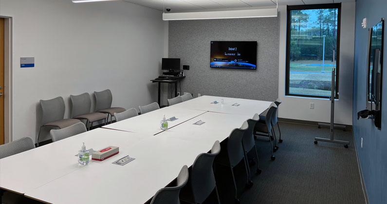 Long conference table, chairs and large flat screen monitors in the PCOM South Georgia Sim Center's debriefing room