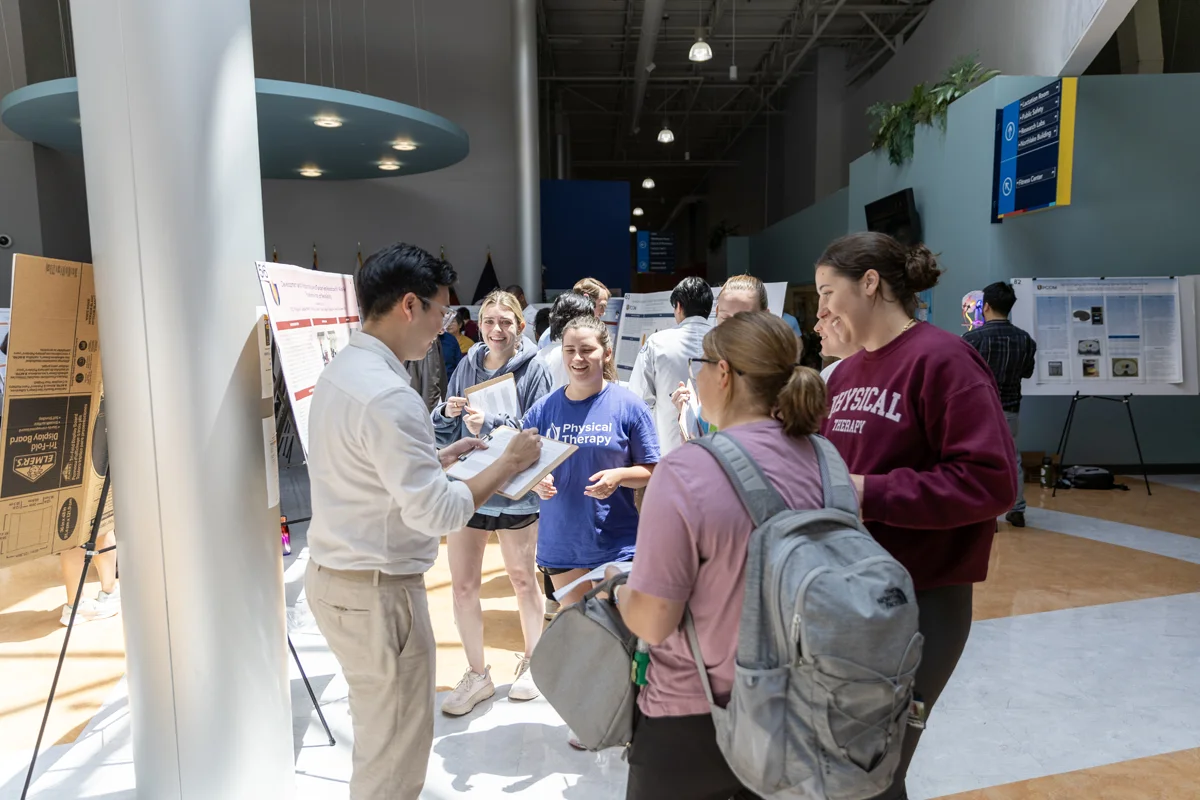Students talk around research posters during the Research Day event in the Atrium