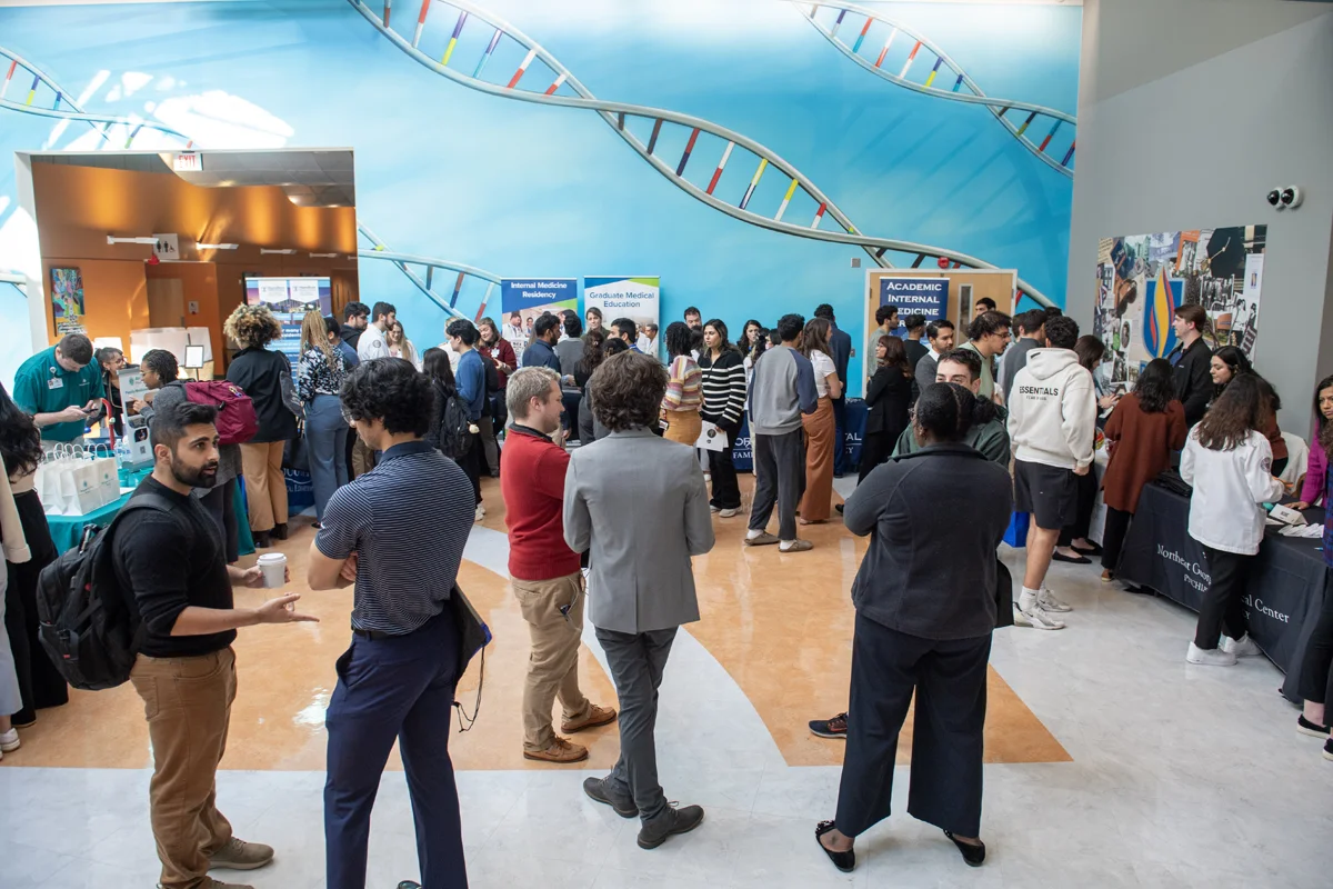 A large group of students and staff talk around information tables during a residency fair event in the Atrium at PCOM Georgia