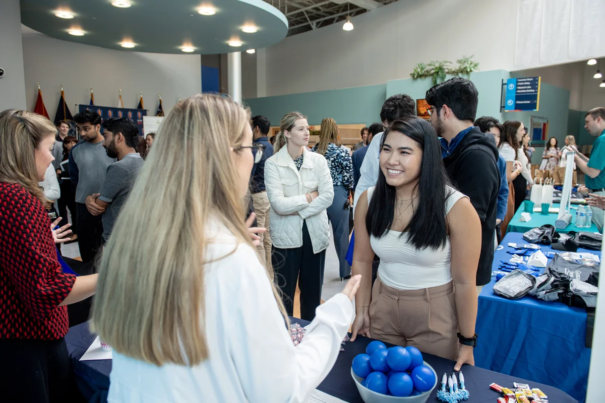 Students smile and talk around information tables during a residency fair event in the Atrium at PCOM Georgia
