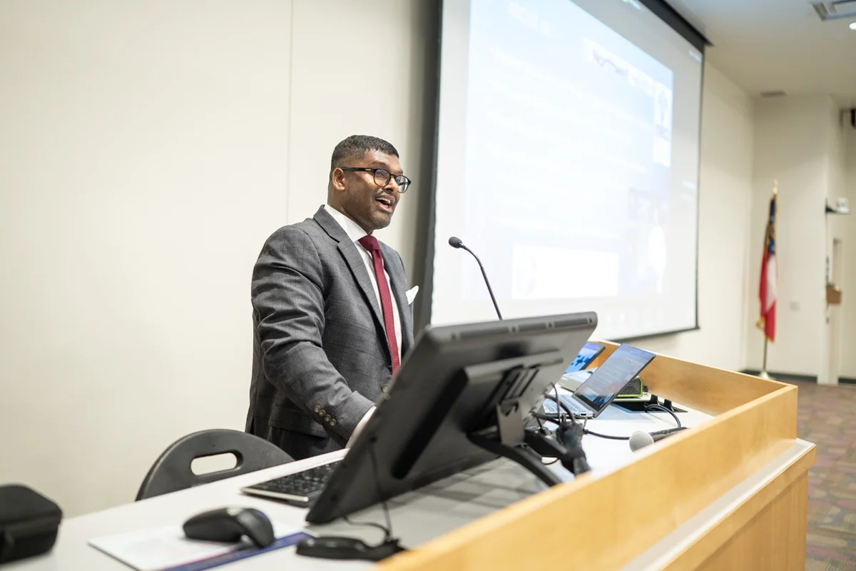 A student presenting in front of a projector screen in a classroom at PCOM Georgia