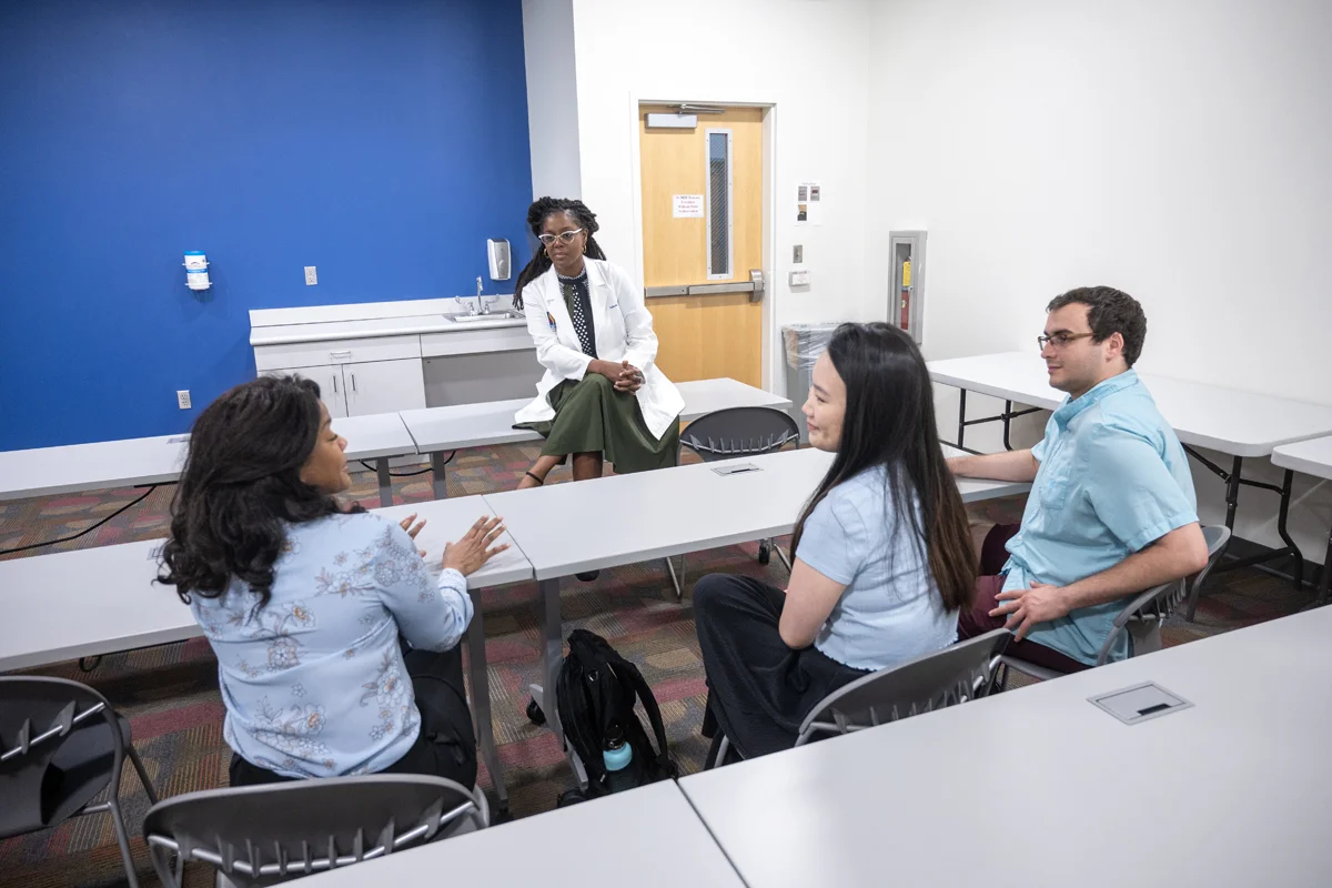 Students sitting on tables and chairs while talking with a faculty member in a smaller classroom at PCOM Georgia