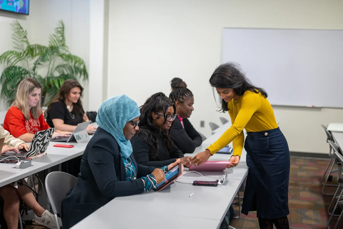 A faculty member walks and helps students sitting at tables in a PCOM Georgia classroom