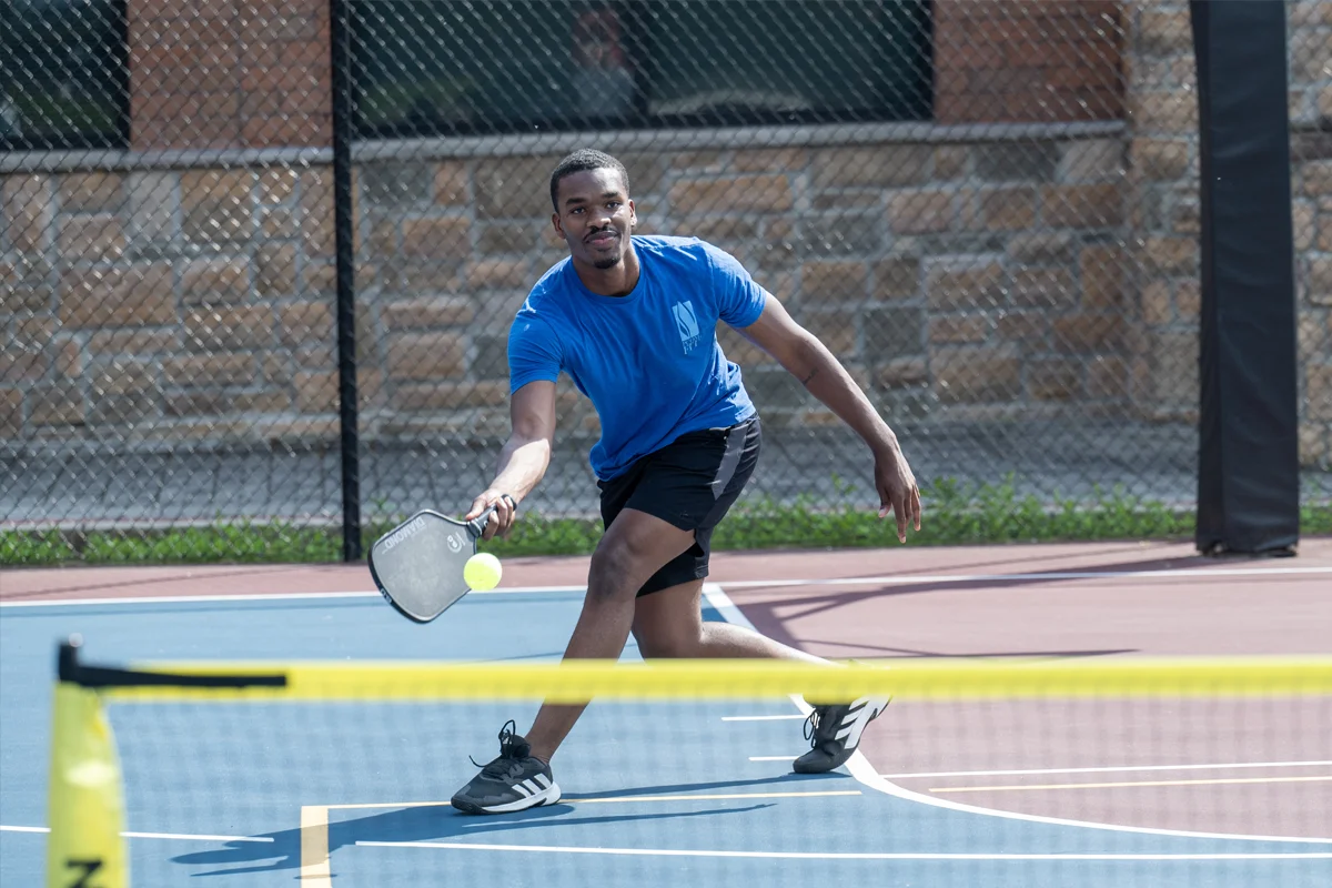PCOM student smiling as he swings a pickleball paddle on the sports court