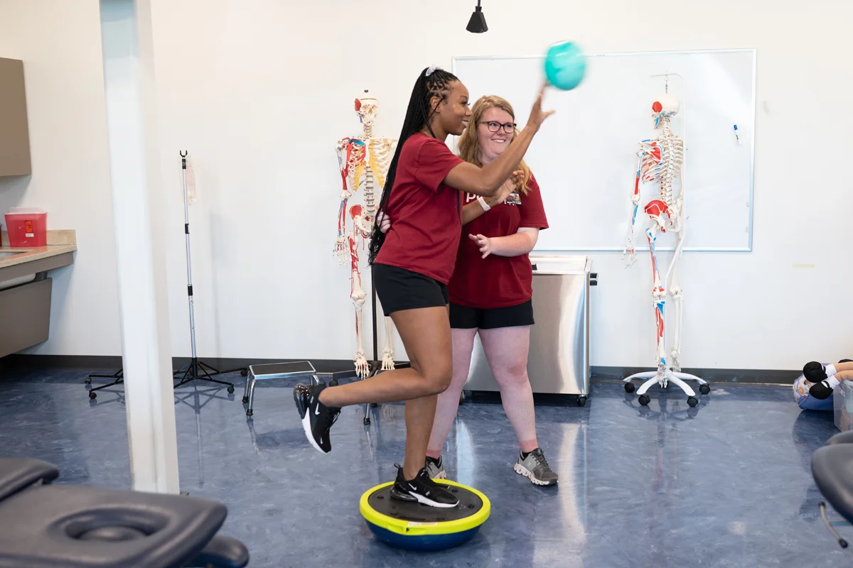 Physical therapy students smile while performing a balance exam exercise