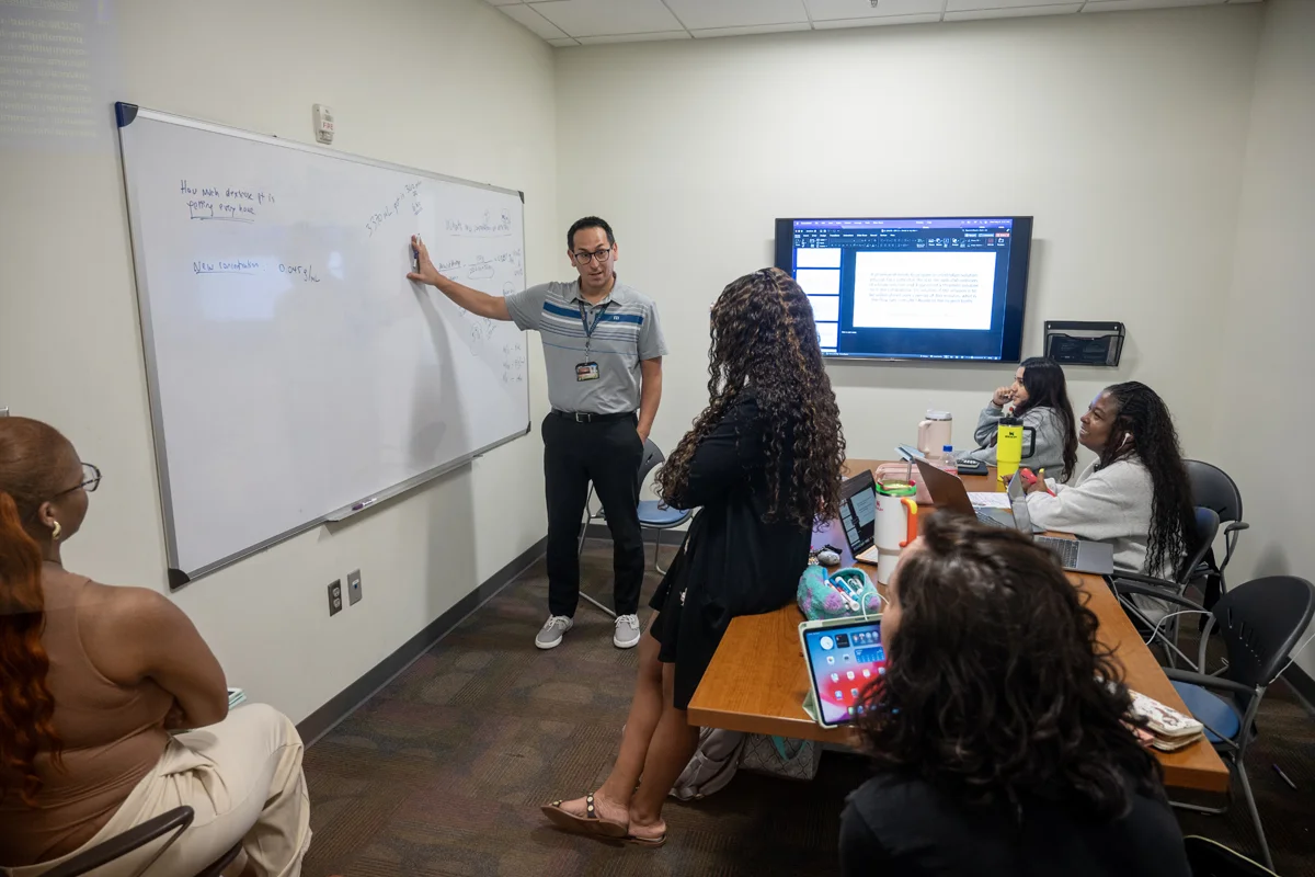 PCOM faculty and students talking in a study room in the Information Commons