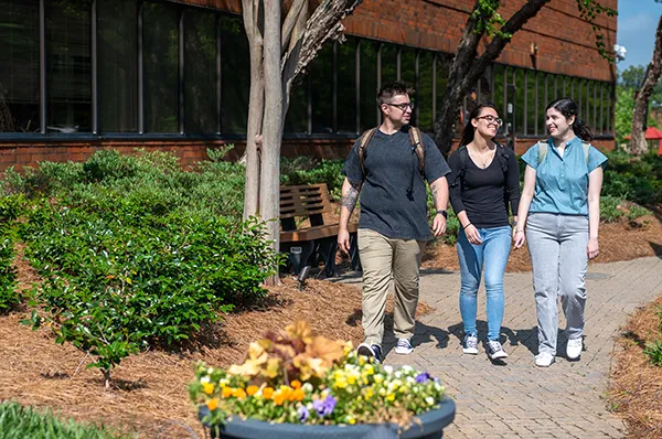 Grad students smile as they walk and talk on a front pathway at PCOM Georgia