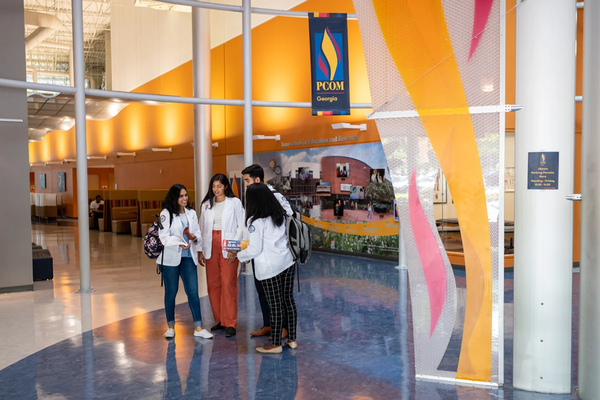 Students talking and looking at a book within the main lobby at PCOM Georgia