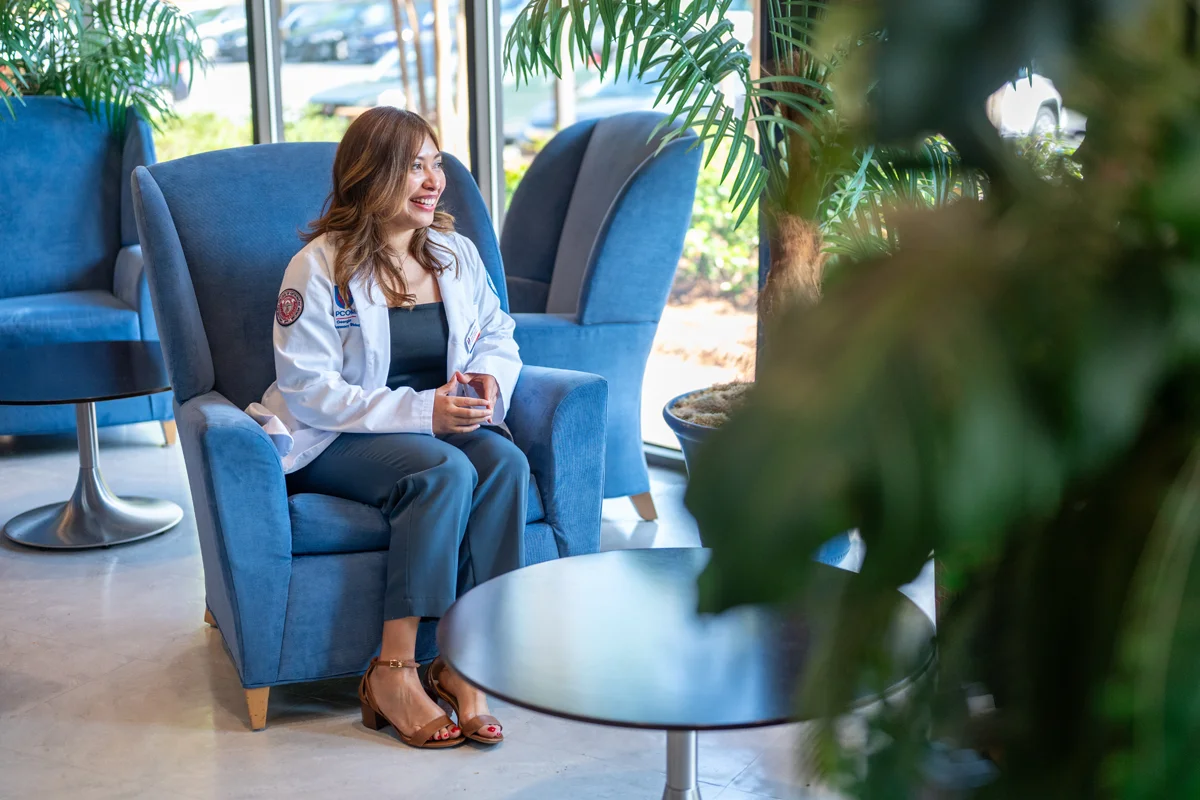 A student smiles while sitting on a chair facing the fron window of the lobby