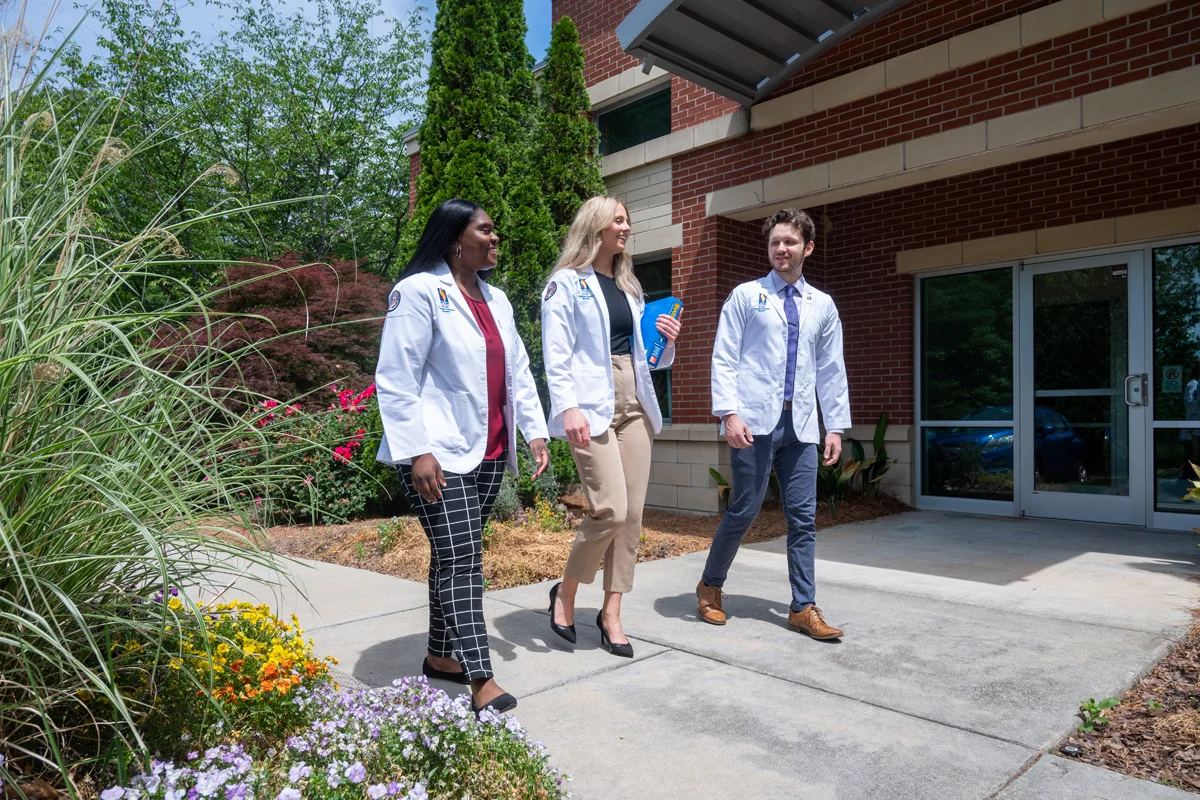 Physician assistant students smile and talk in front of the Northlake building