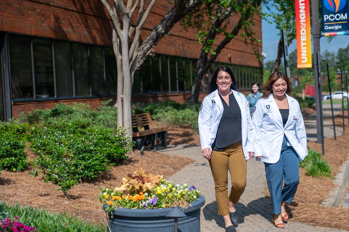 Med students walking and smiling on the side pathway of PCOM Georgia