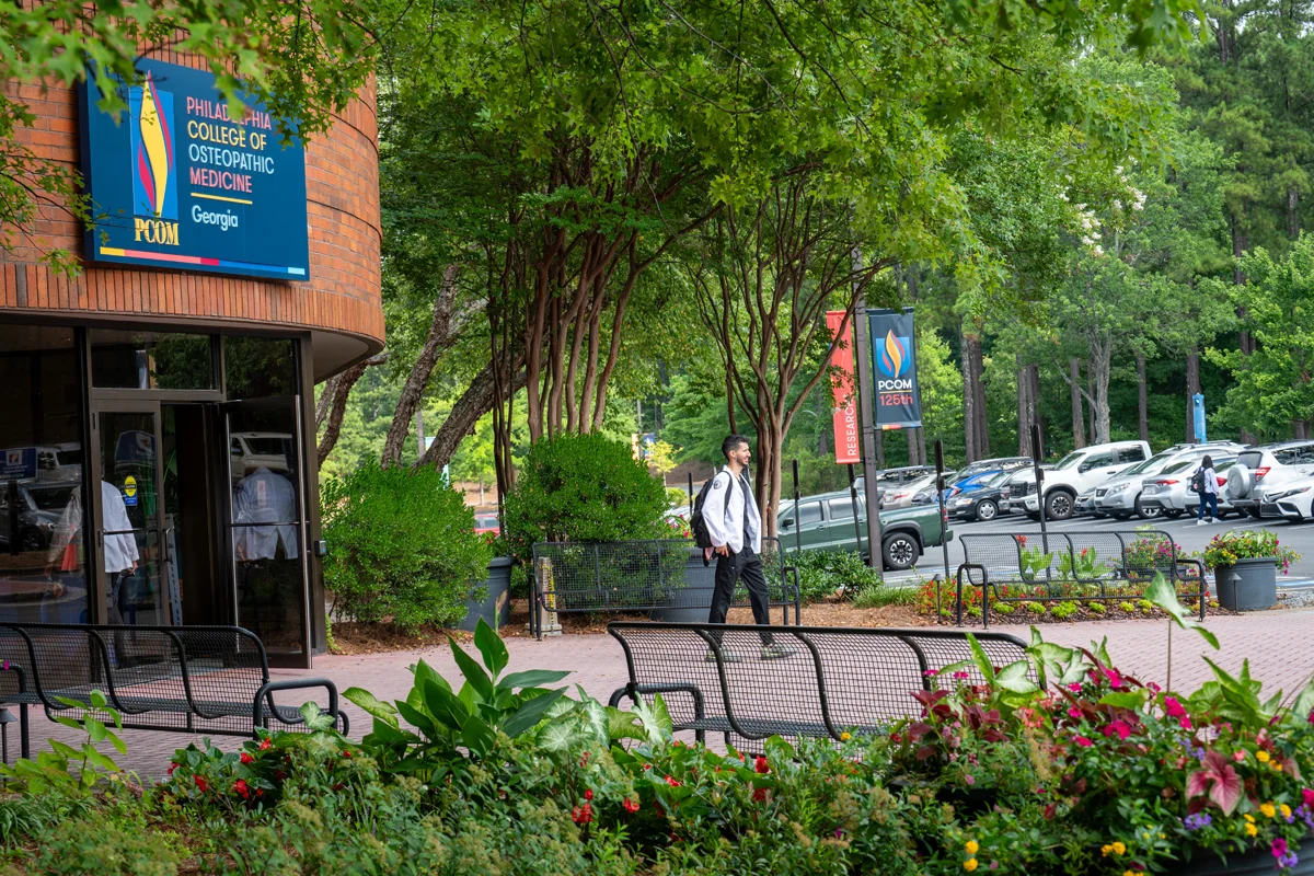 A student walking out of PCOM Georgia's main building front doors with flowers and landscaping