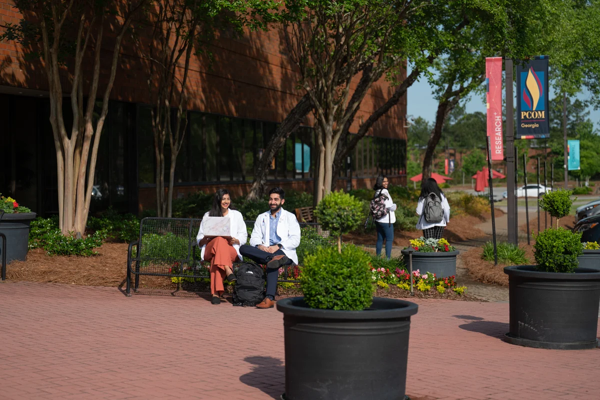Students smiling and talking on a bench in front of PCOM Georgia