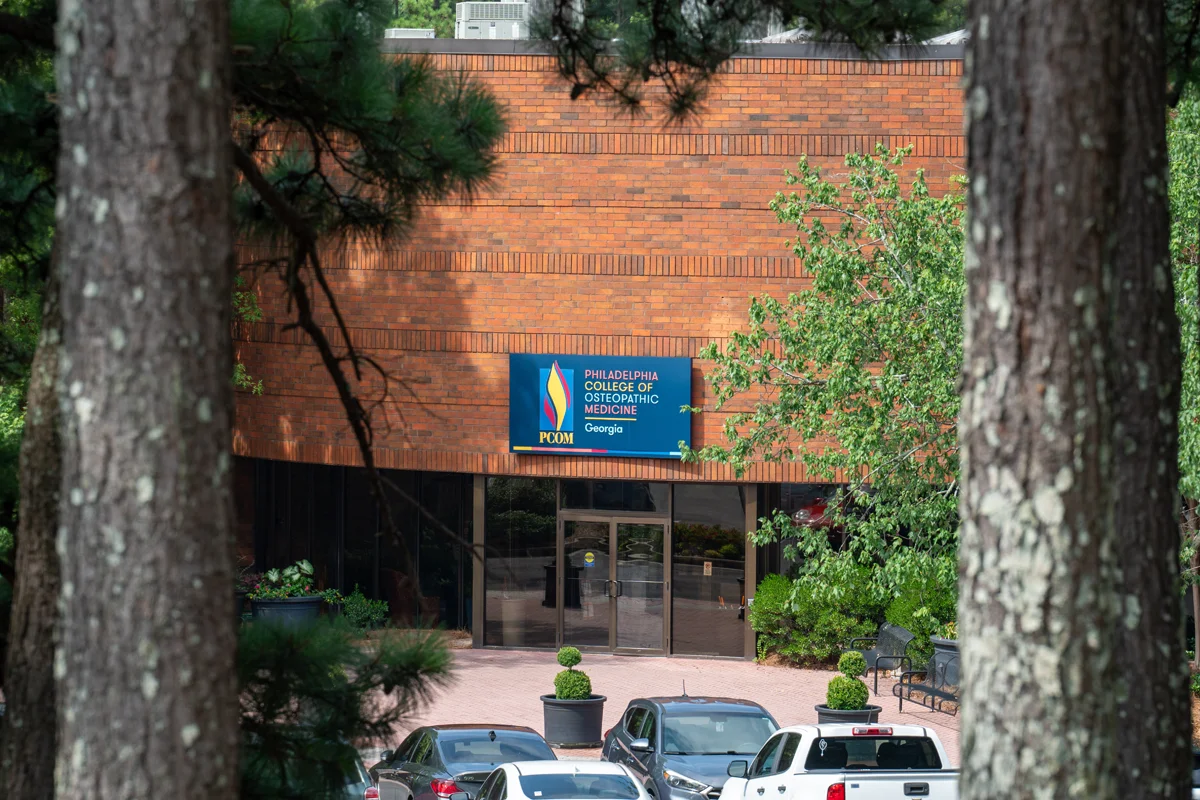 Artistic shot of PCOM Georgia's front doors through two pine tree trunks