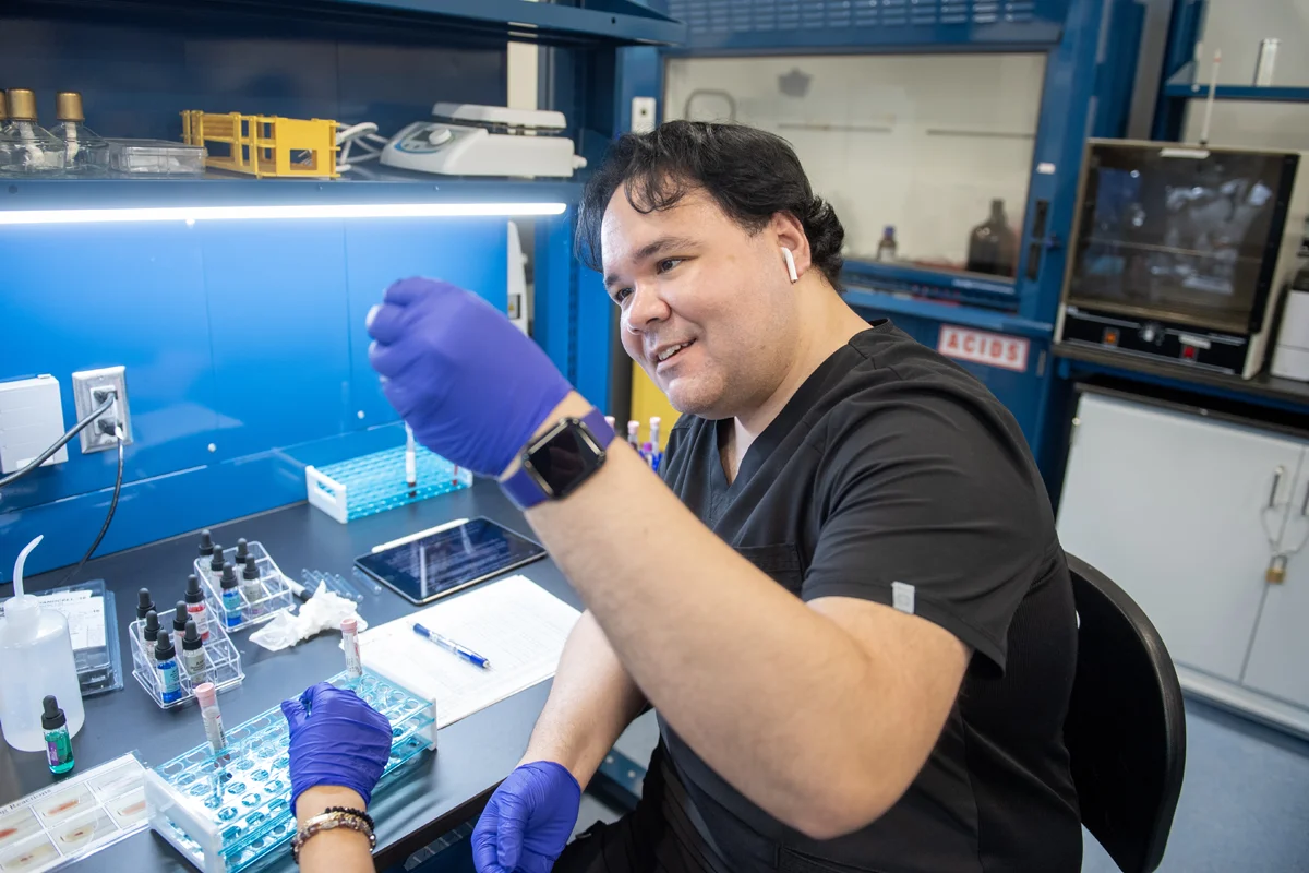 A medical lab science student smiles while looking at a mixture in a lab