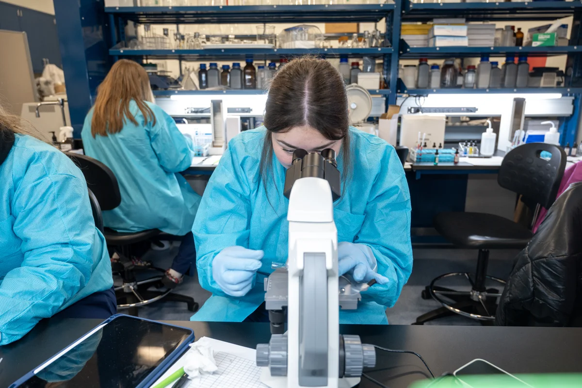 Biomed student in scrubs using a micrscope in a research lab