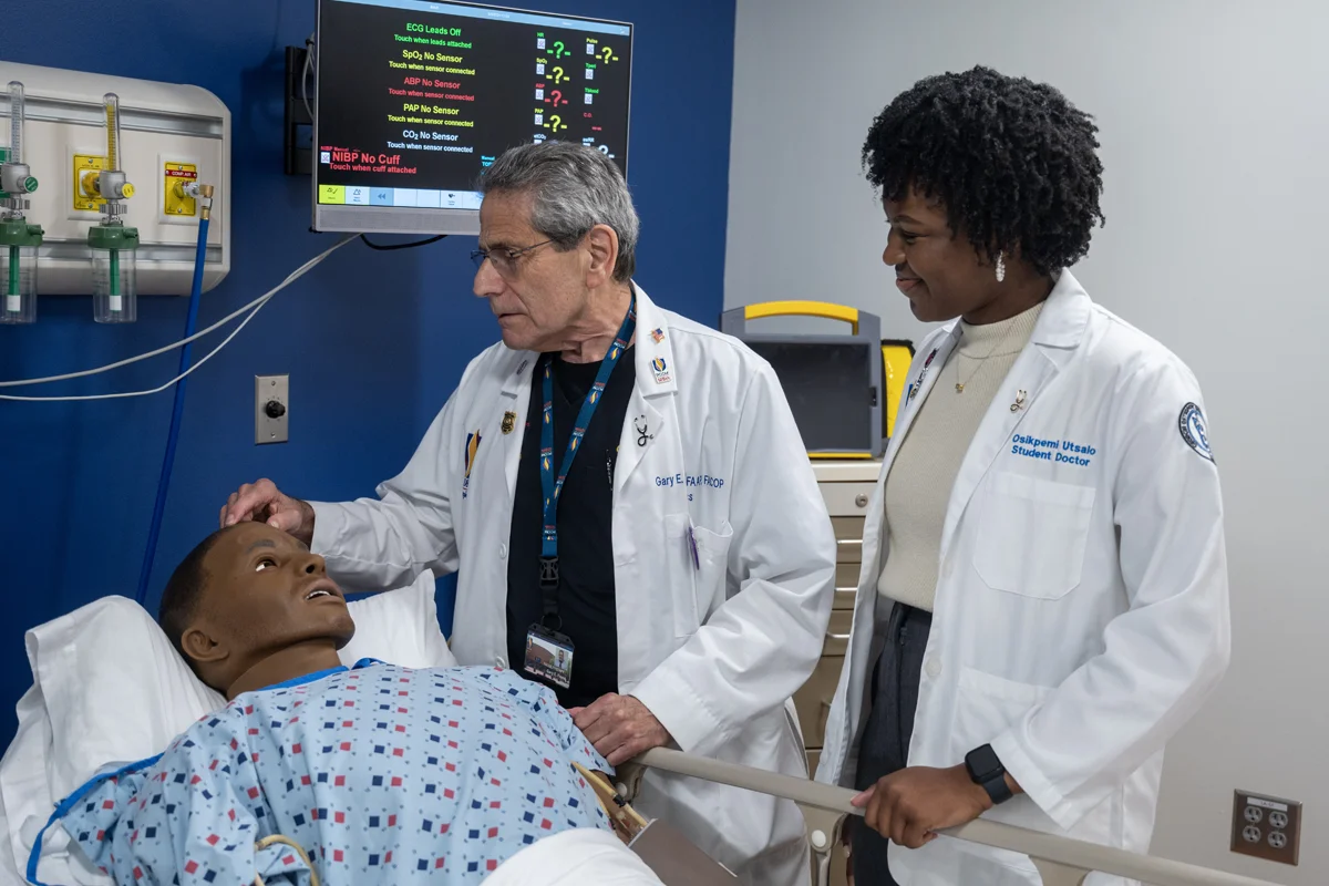 PCOM Georgia faculty and student examine a black patient sim mannequin