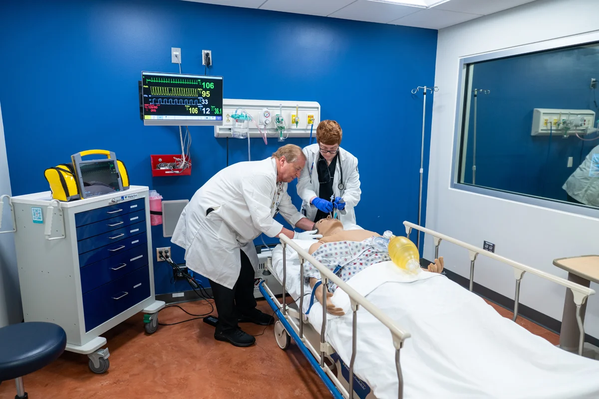 PCOM Georgia med student and faculty member tend to a mannequin patient on a hospital bed