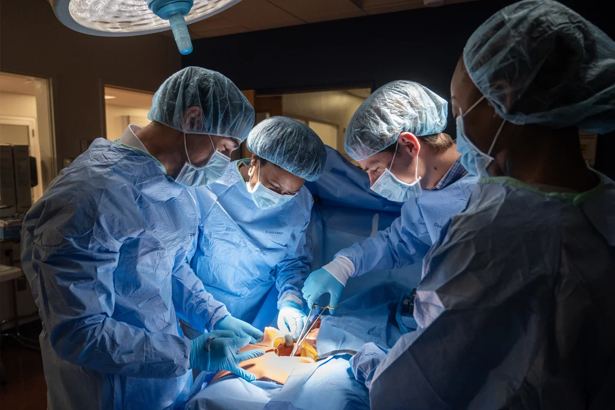 Med students huddle over a simulated patient mannequin on the surgery simulation table