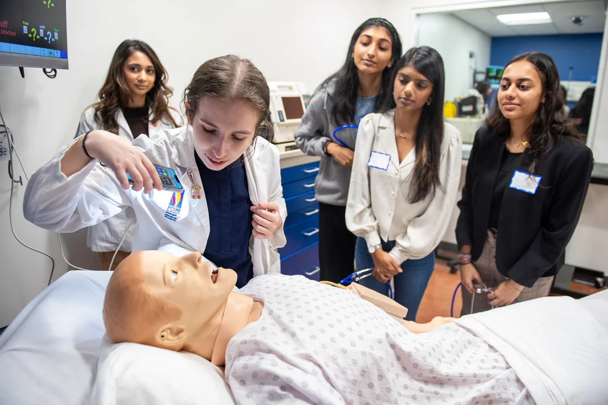 Students examine a mannequin on a hospital bed