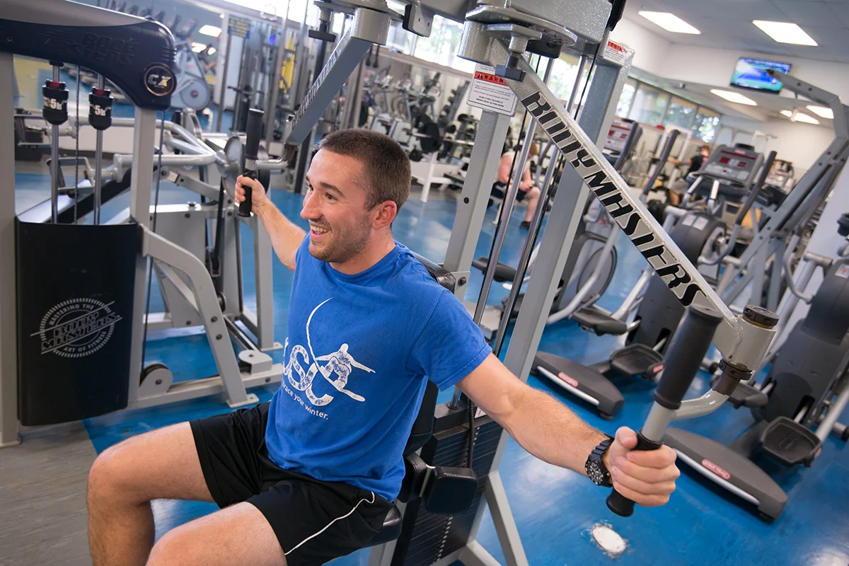 Grad student smiling as he uses exercise equipment in the weight room