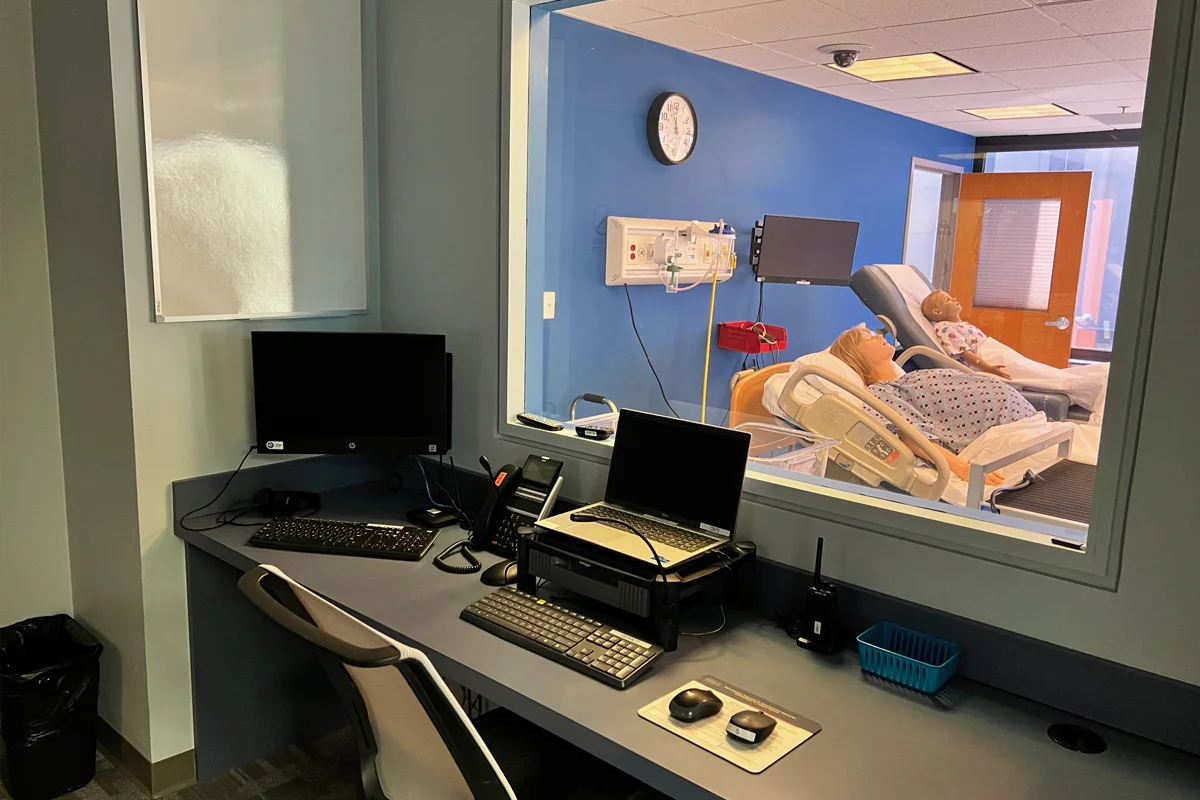 Control room within the CLAC with a wide window into a practice room, computer monitors and AV equipment