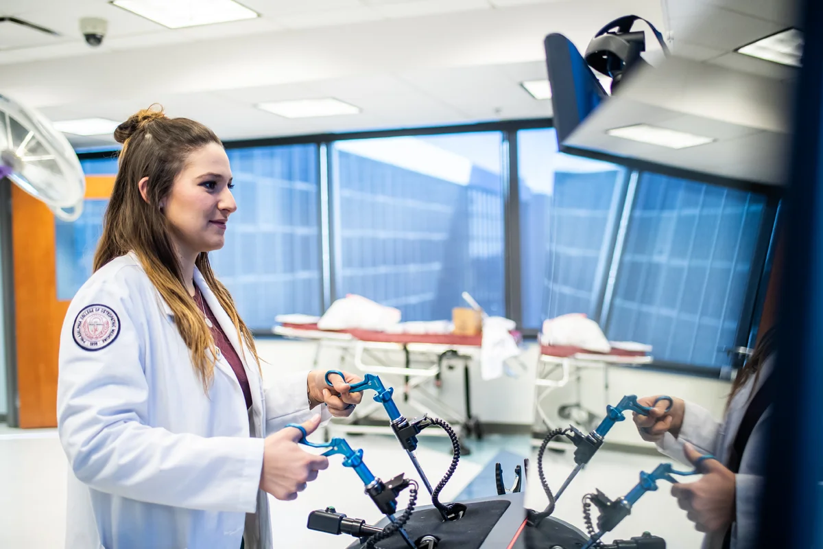 Med student smiling as she uses simulation equipment in the CLAC