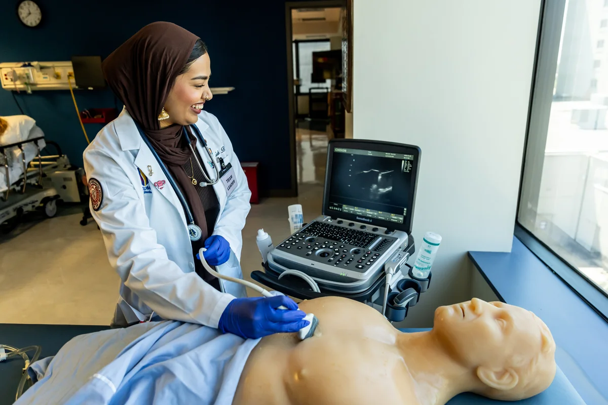 A med student smiles as she uses simulation equipment on a robotic patient torso