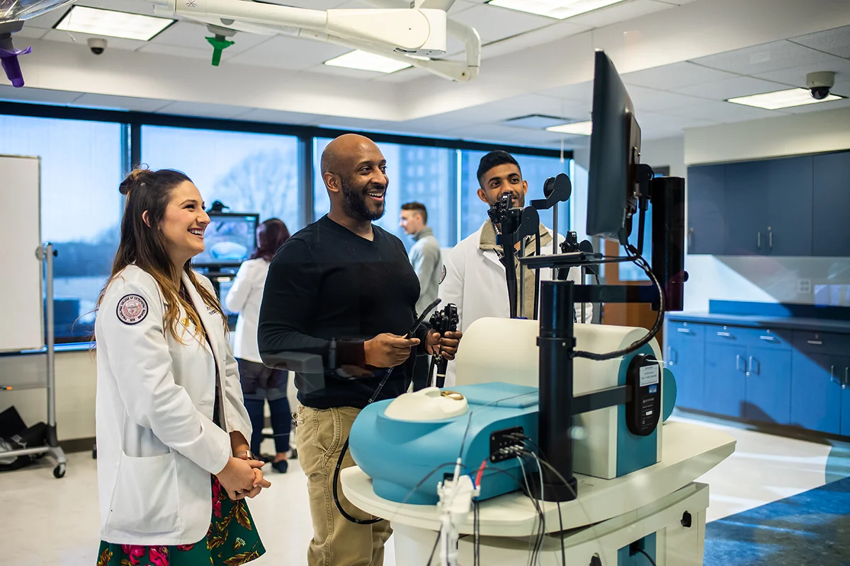 PCOM staff and med students smiling while with surgery simulators in the Sim Center