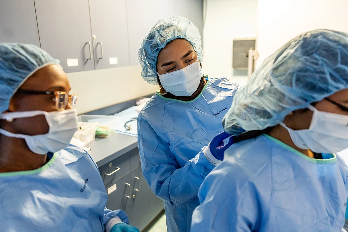 A medical student helps a peer put on PPE before a surgery exercise