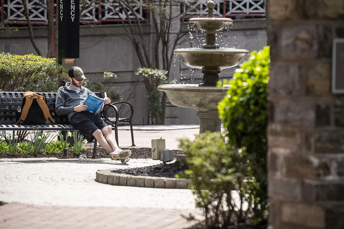 A PCOM med student studying a medical textbook on a bench next to the fountain