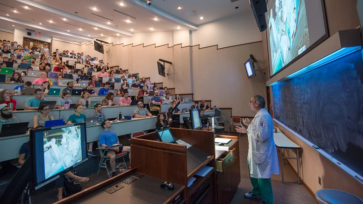 Rows of students sit and listen to a PCOM faculty member in one of the large amphitheatre lecture halls
