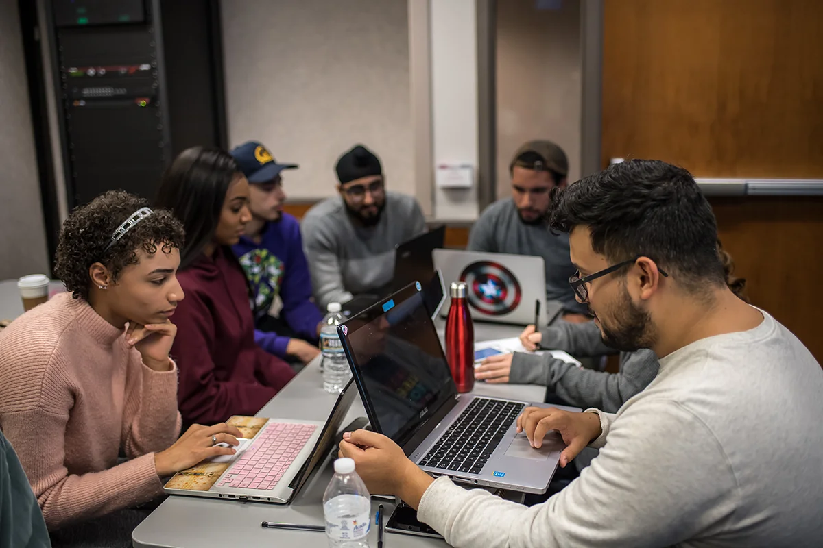 PCOM grad students working together on laptops around a table within a classroom in Hassman