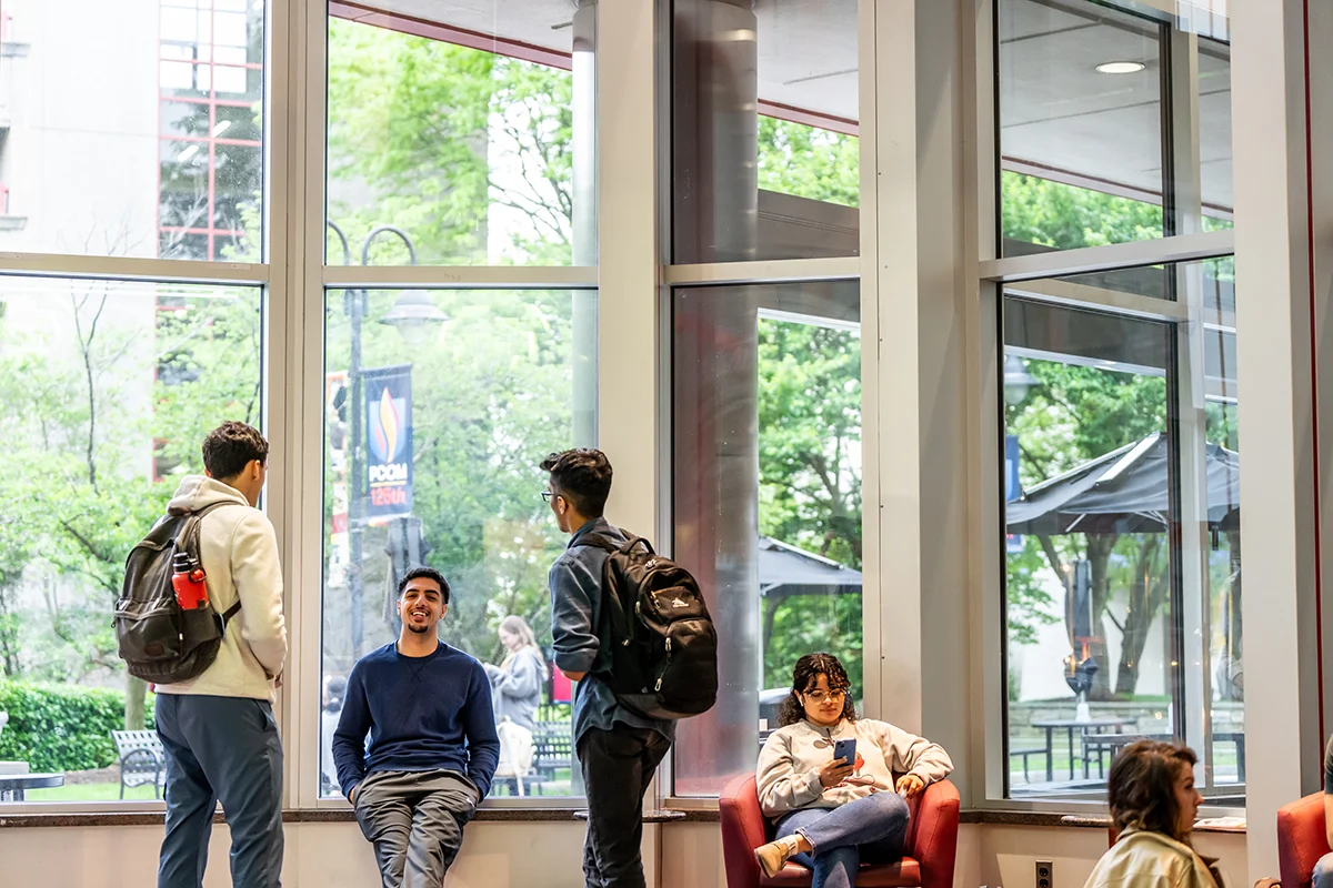 Students smiling and studying near the large front windows of the Hassman building lobby