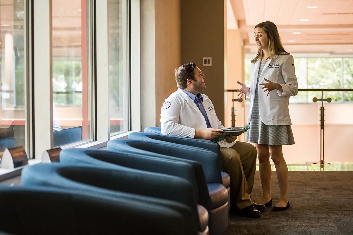 Two DO students smiling and talking in a common area within the Hassman building