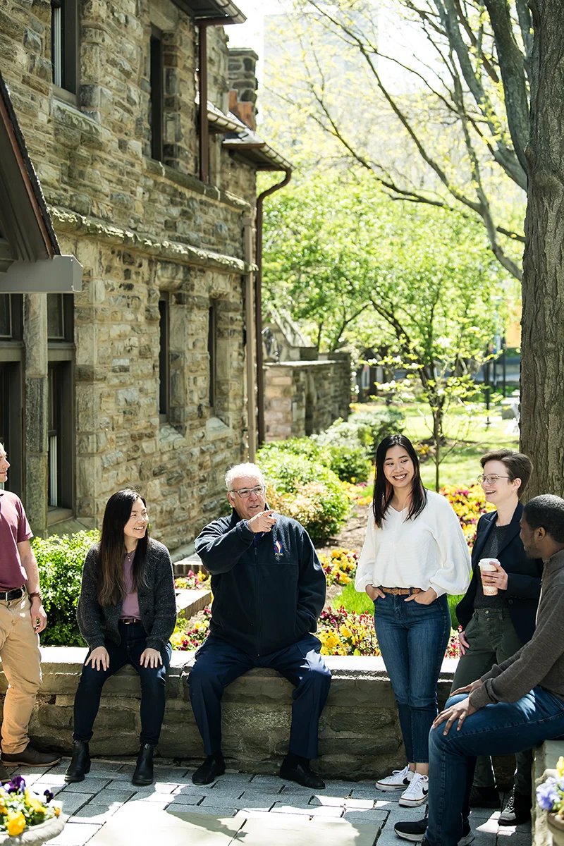 PCOM's president Dr. Feldstein and students sitting and talking in front of the Levin building