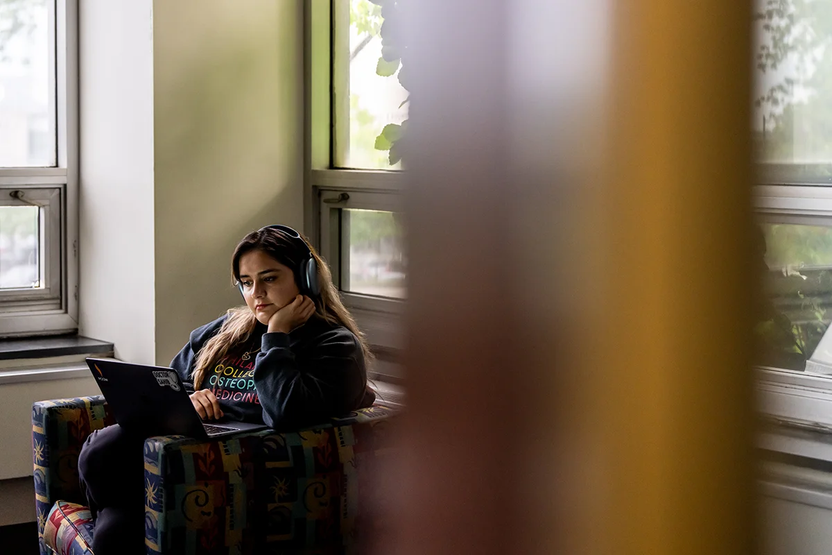 Student studying on a laptop while sitting on a chair in the PCOM Library