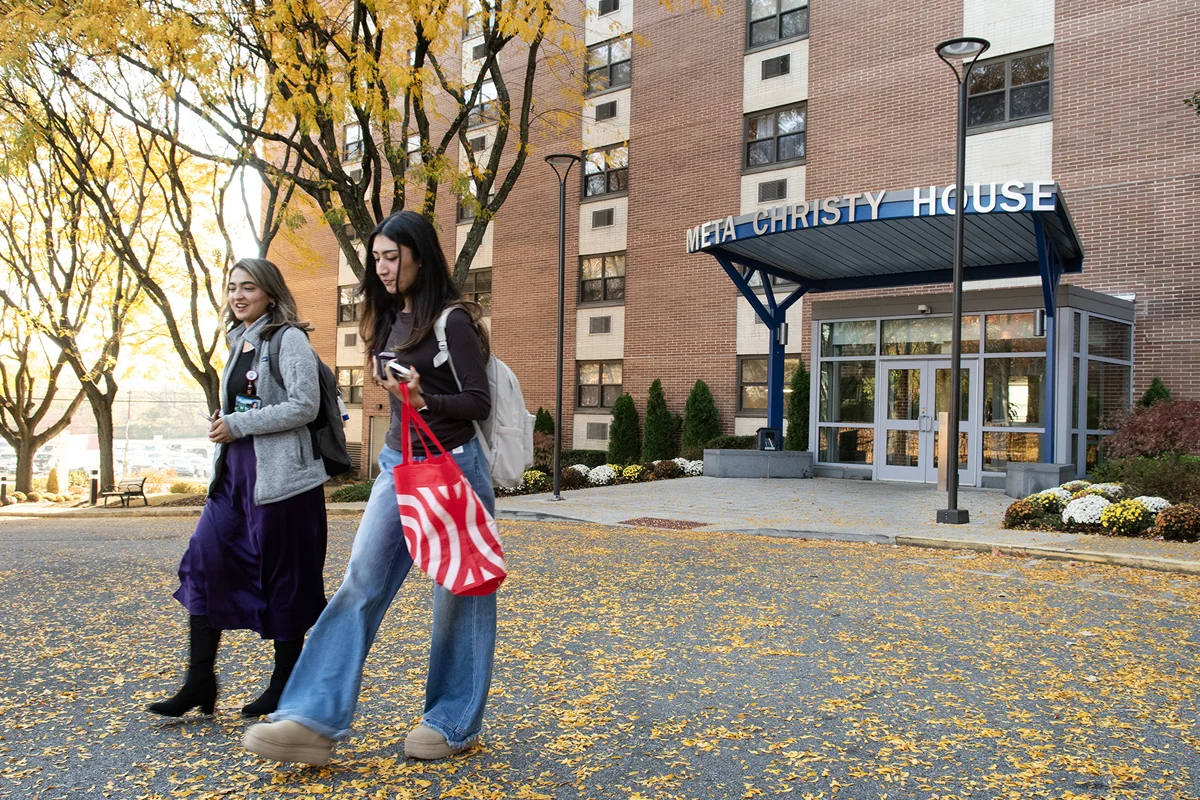 Grad students smiling and talking as they walk out of the Meta Christ House front doors during autumn