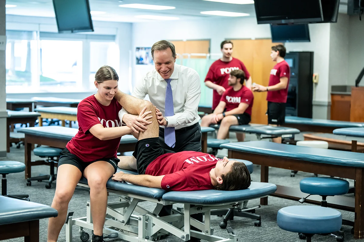 PCOM faculty and students smiling while practicing OMM techniques in the lab