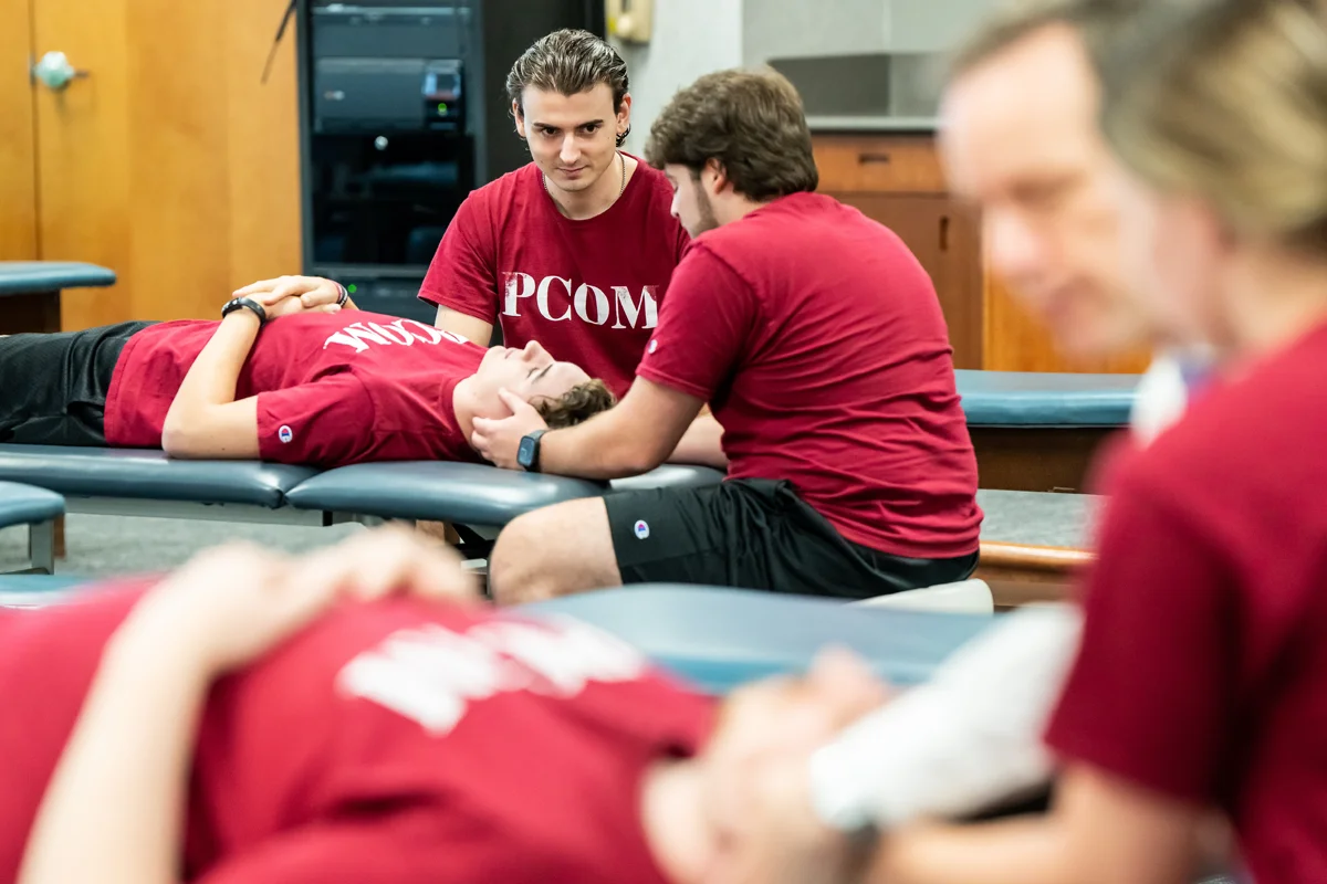 Students smiling while practicing OMM techniques in the PCOM classroom space