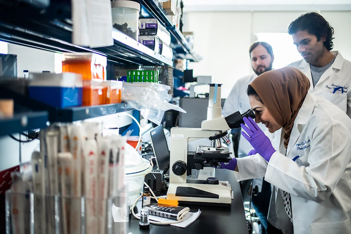 Students smiling as they look through a microscope in one of the research labs