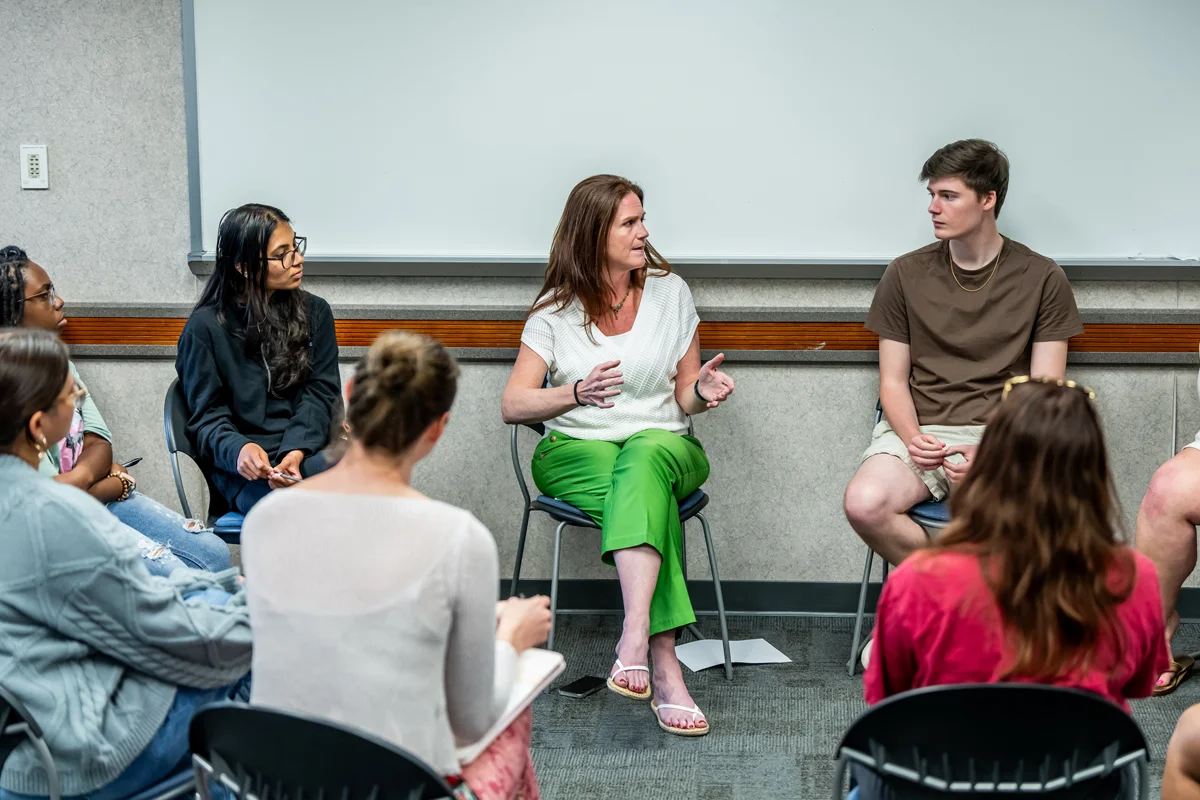 Students and faculty talking in a circle of chairs in a classroom in Rowland Hall
