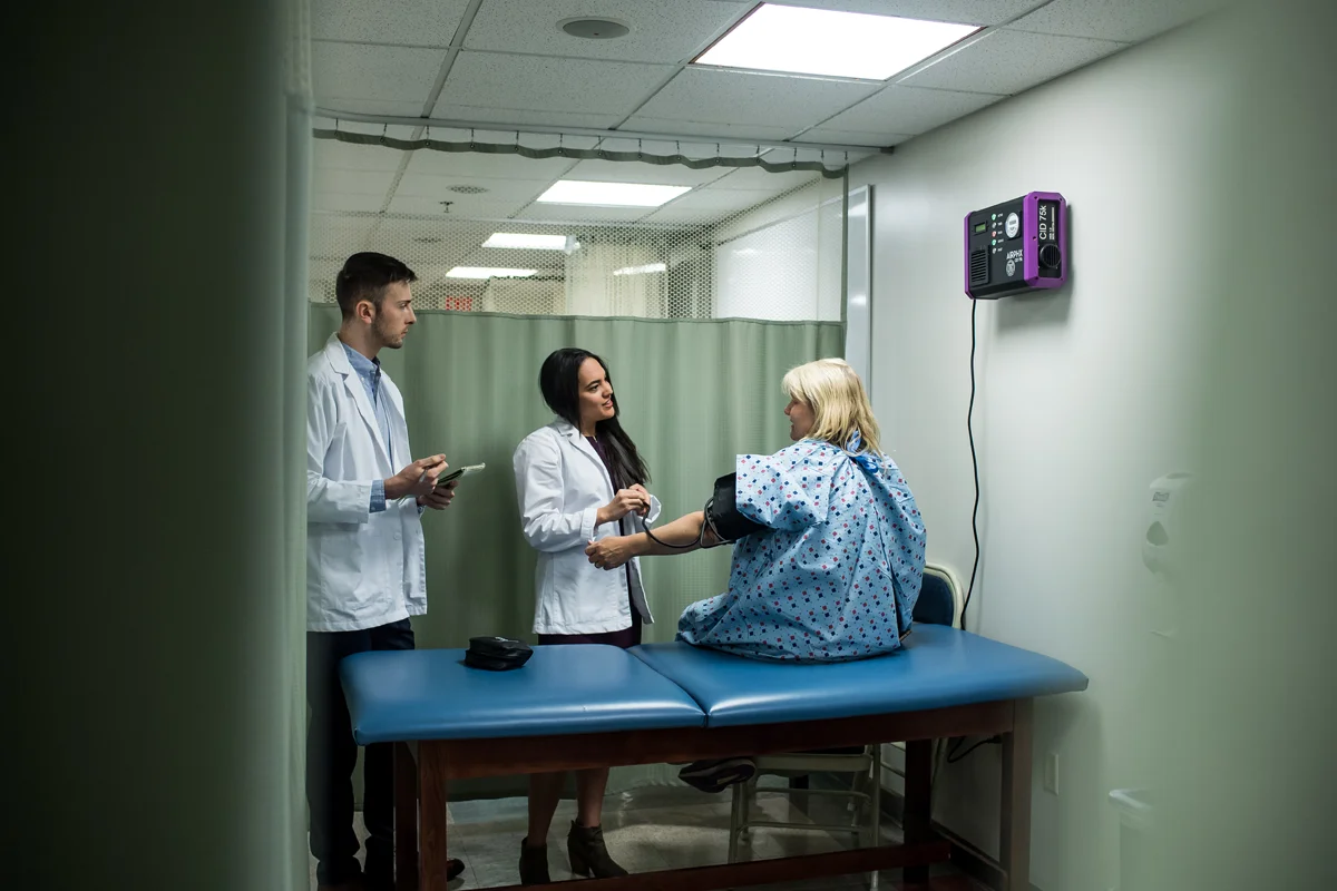 Two PA Studies students taking the blood pressure of a standardized patient actor